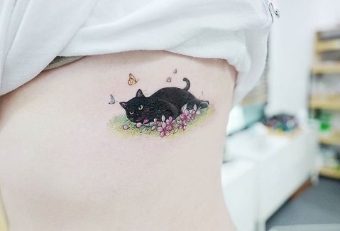 Tatuagem gato preto deitado sobre flores com borboletas voando